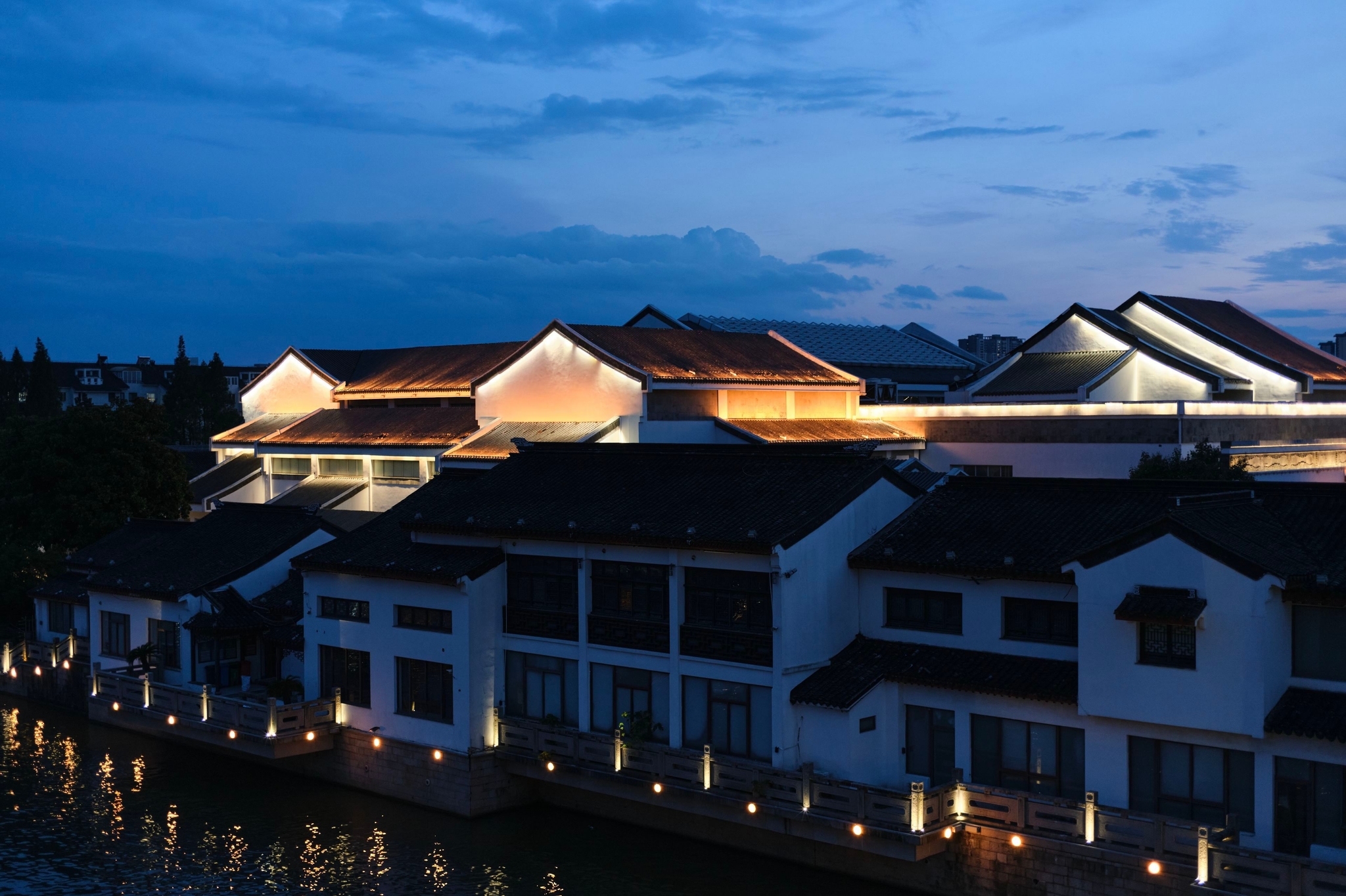 Traditional buildings illuminated at night along a waterway under a dark blue sky
