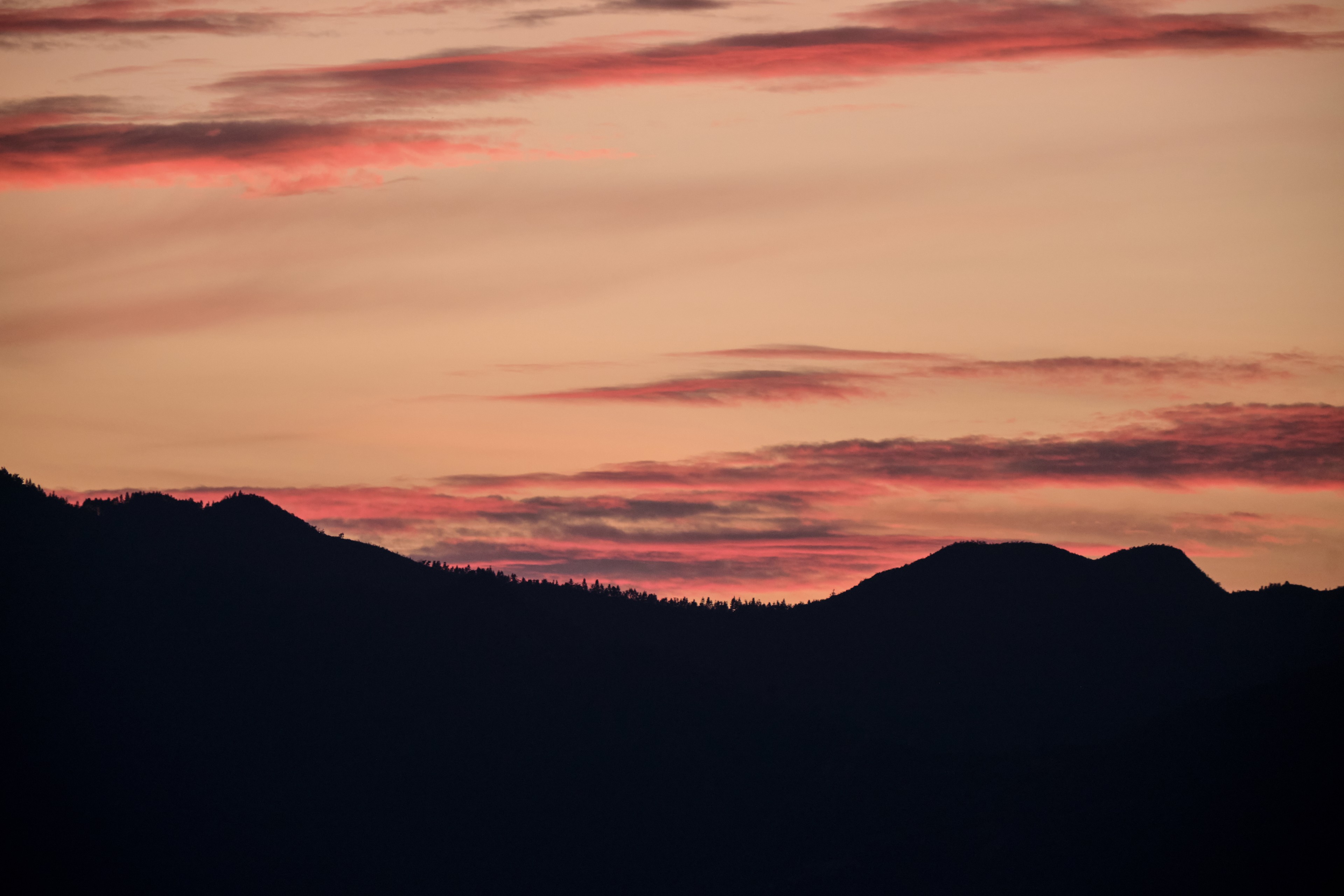 Dark mountain silhouettes against a vibrant sunset sky with red and orange clouds