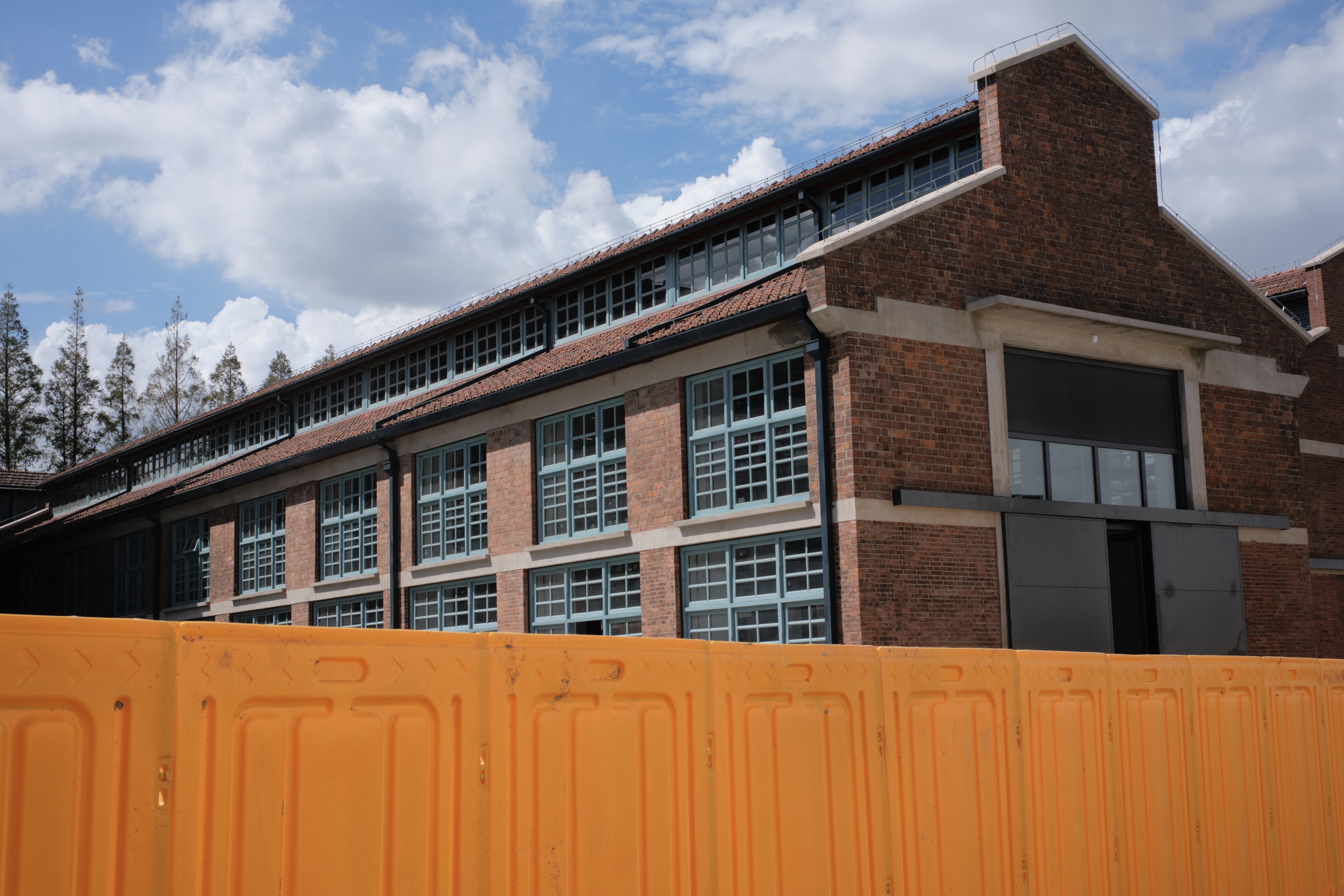 Brick building with numerous windows behind an orange barrier under a cloudy sky