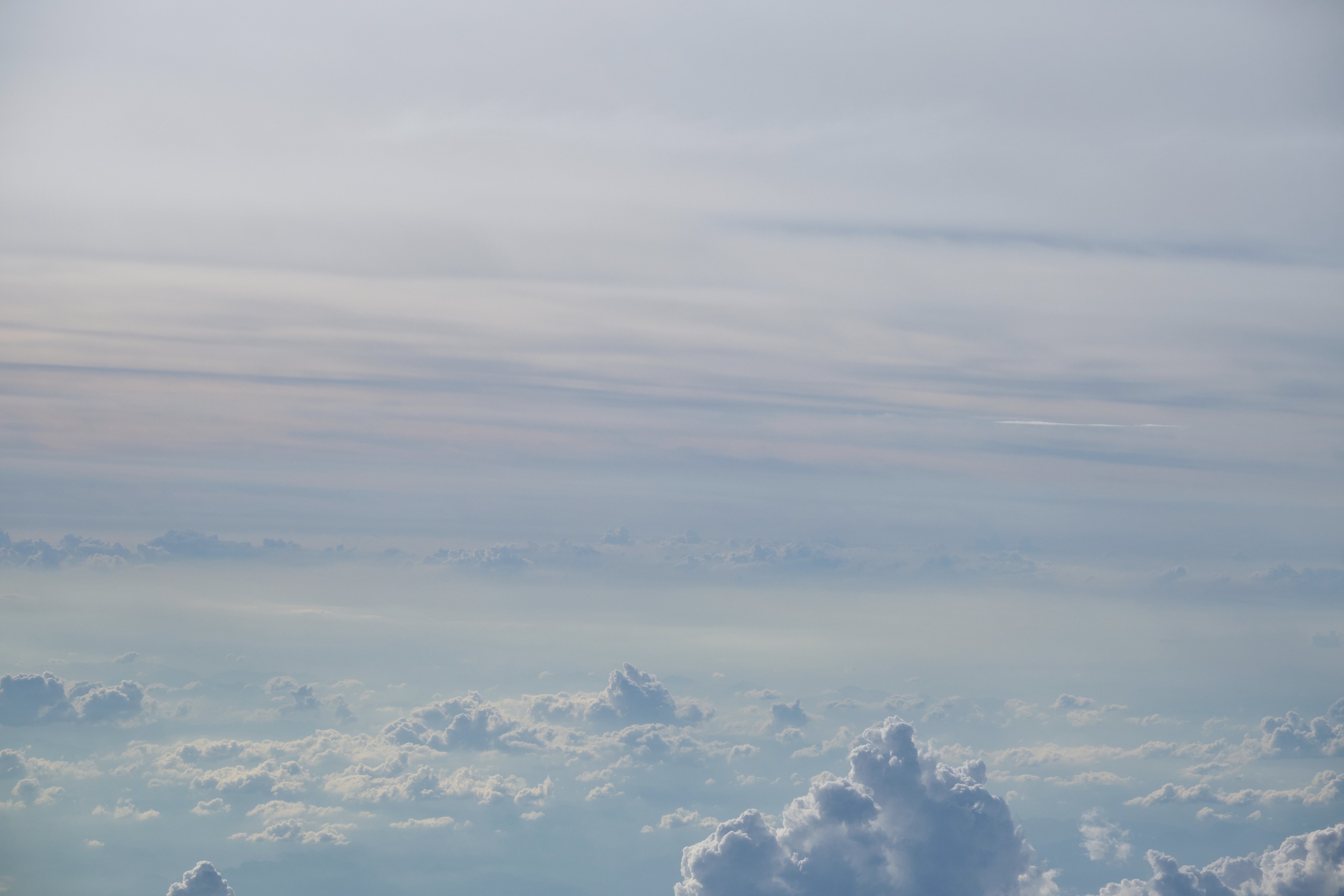 Layered clouds from above, pale blue-grey sky dominating the frame