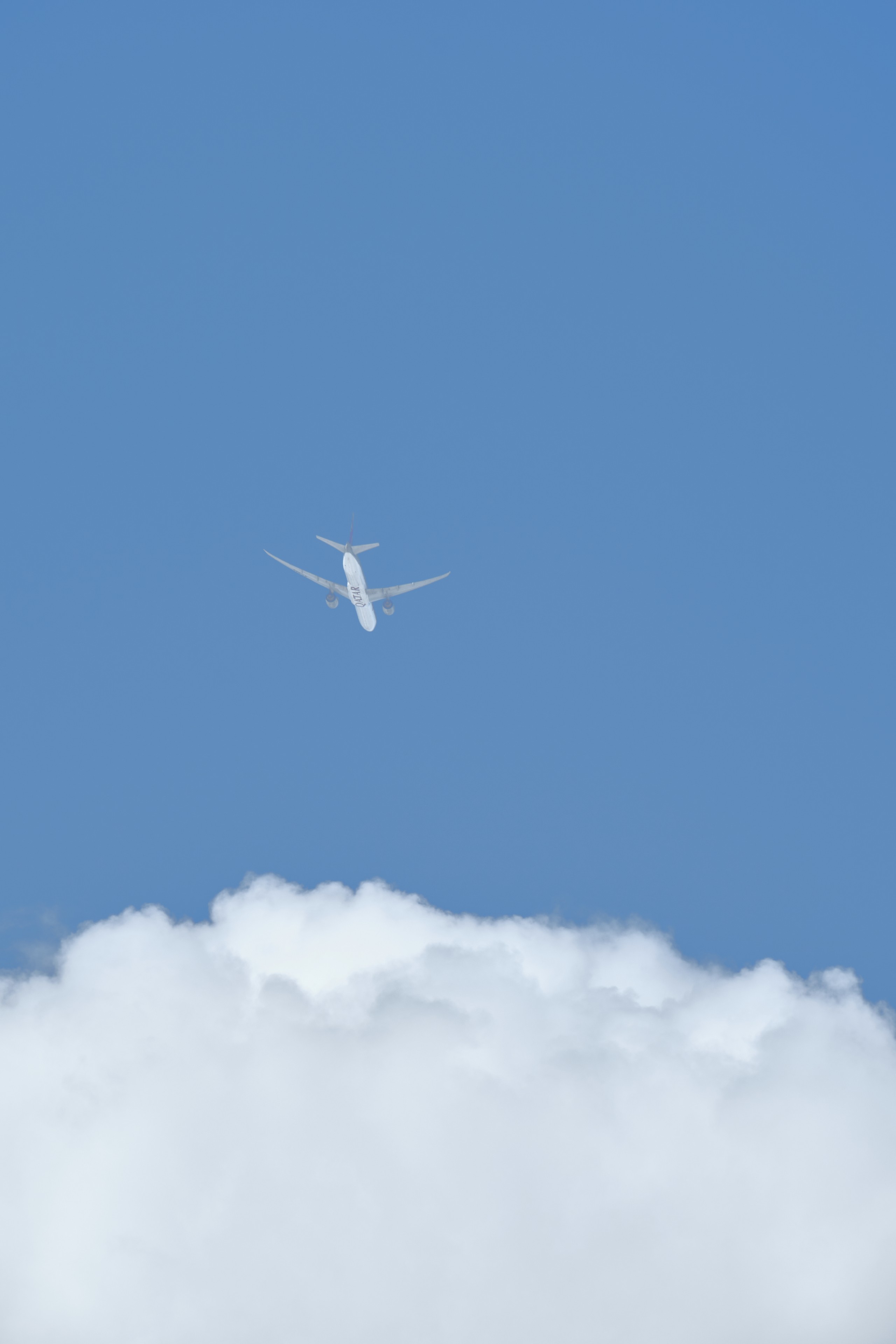 White airplane flying above clouds in a blue sky
