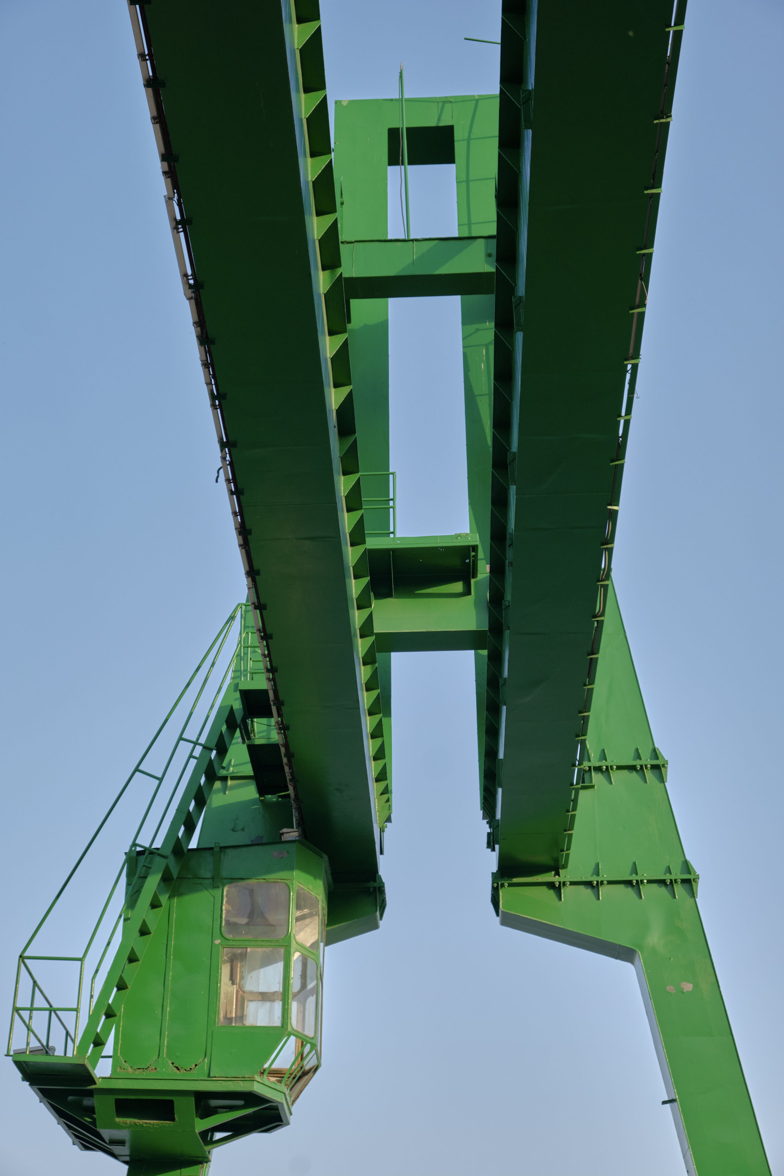 Large green industrial gantry crane viewed from below against a clear blue sky