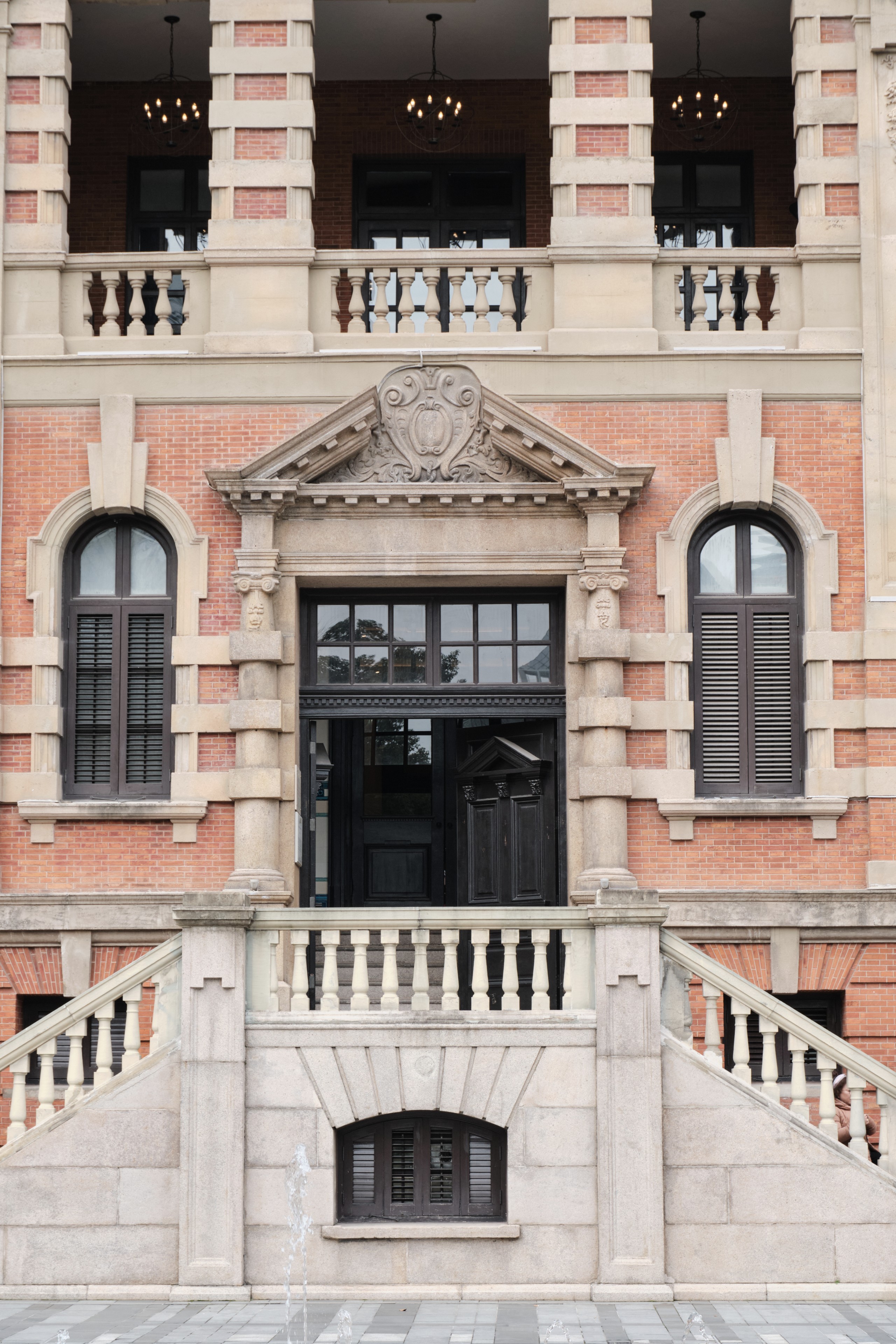 A symmetrical view of a neoclassical building facade featuring a central entrance elevated by stone steps with balustrades, arched windows, and a brick-and-stone exterior