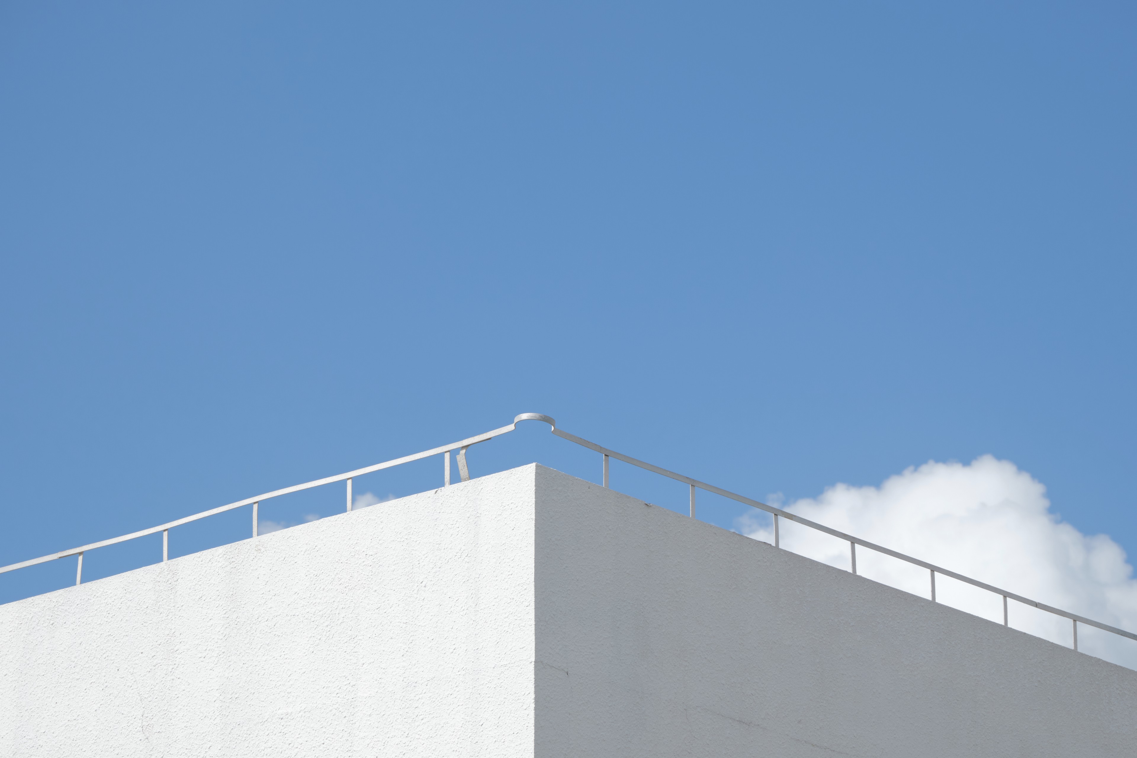 White building corner and railing against a blue sky with a single white cloud