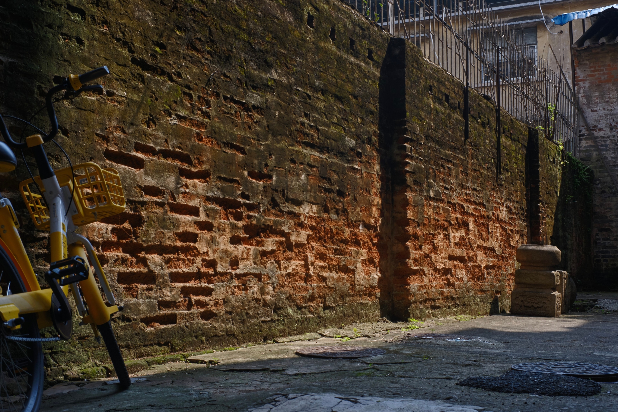 An old, moss-covered brick wall with vertical stone pillars alongside a yellow bicycle