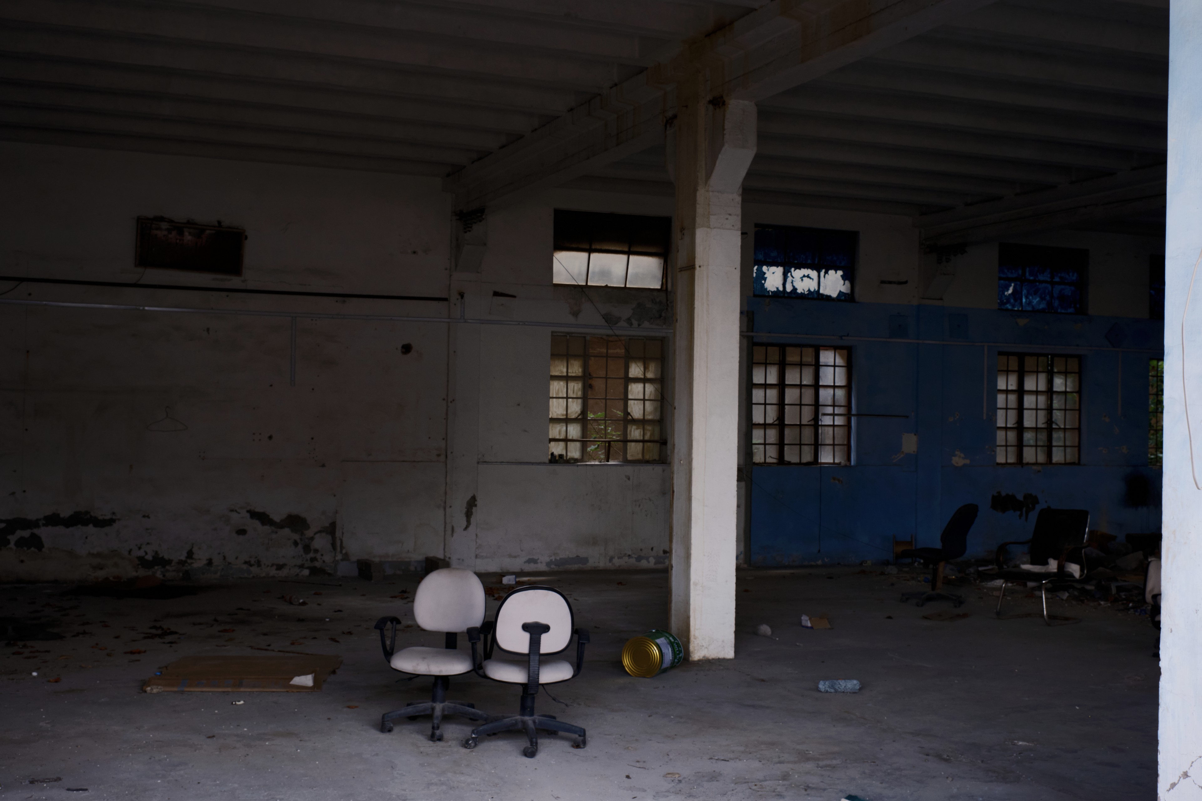 Dimly lit, empty room with two office chairs, a concrete pillar, and gridded windows on discolored white and blue walls
