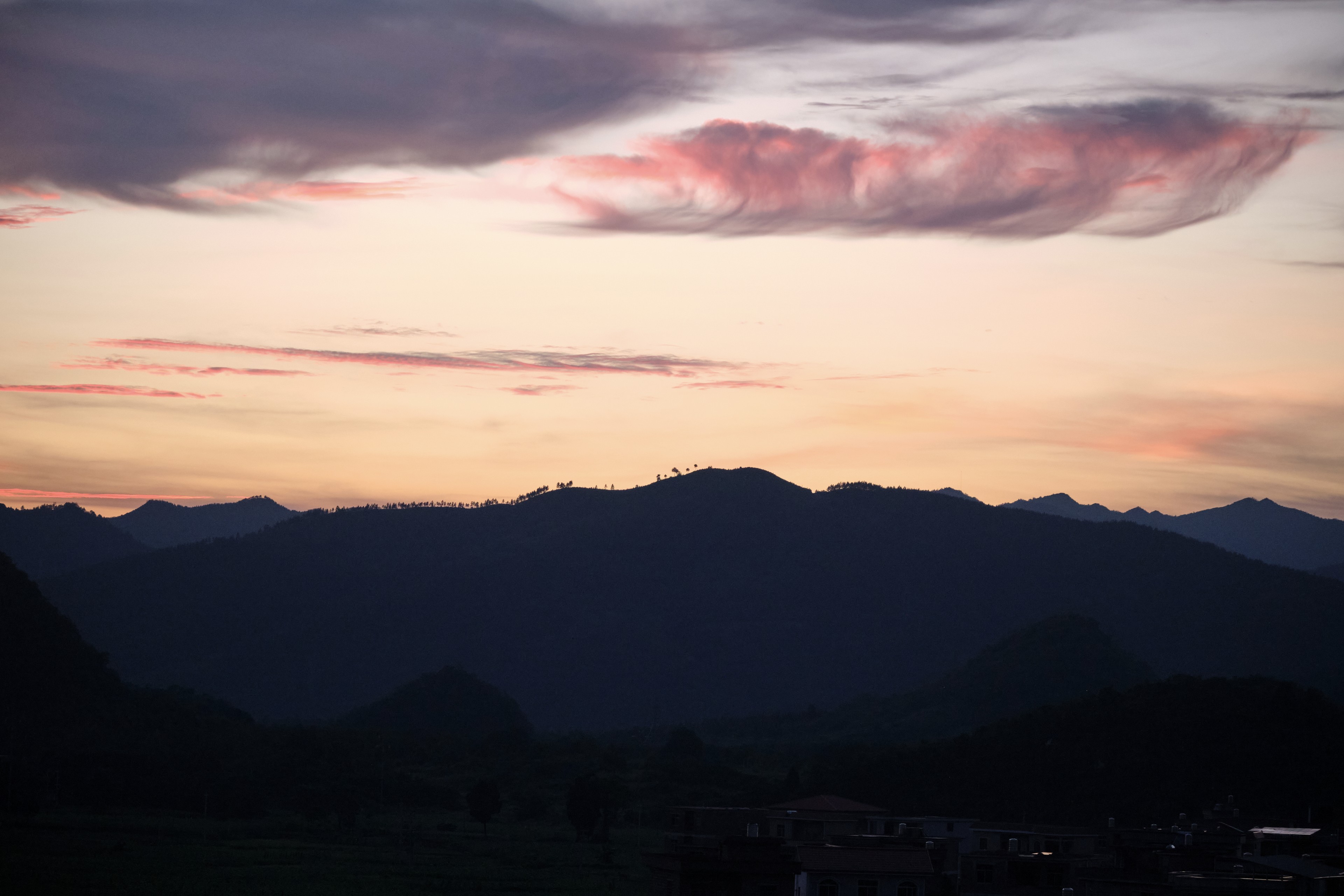 Dark mountain range silhouette against a pastel sunset sky with pink clouds