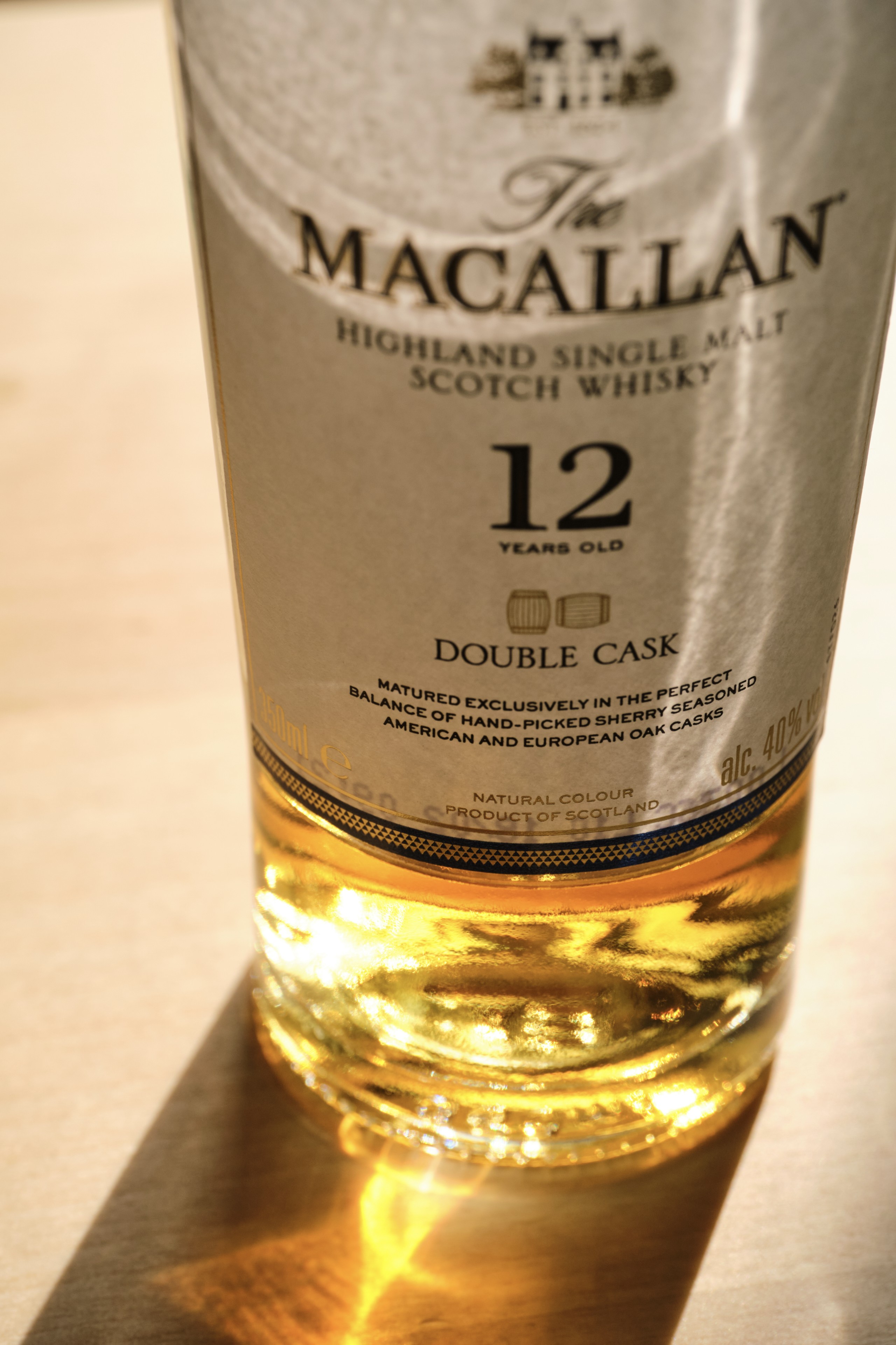 Close-up of a Macallan 12 Year Old Double Cask Scotch whisky bottle showing the label and glowing golden liquid against a light surface