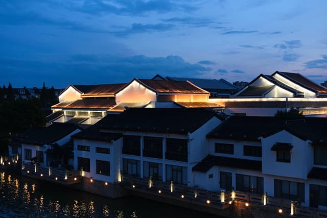 Traditional buildings illuminated at night along a waterway under a dark blue sky