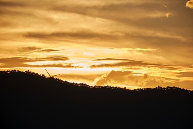 Dark silhouette of rolling hills under a golden sunset sky with luminous clouds