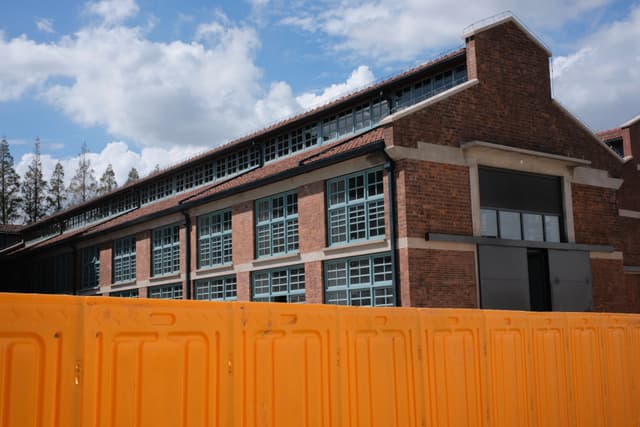Brick building with numerous windows behind an orange barrier under a cloudy sky