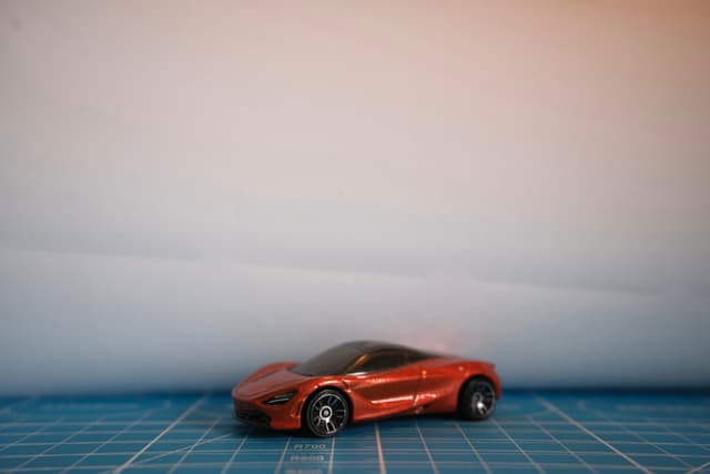 A small red toy sports car positioned on a blue gridded surface against a plain, light-toned background