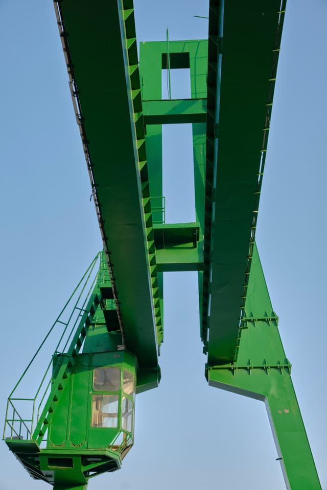 Large green industrial gantry crane viewed from below against a clear blue sky