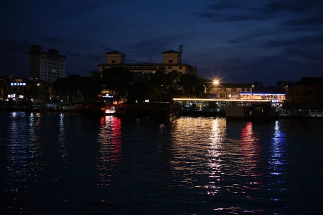Night view of a city waterfront with illuminated buildings reflecting on dark water