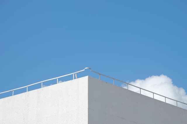 White building corner and railing against a blue sky with a single white cloud