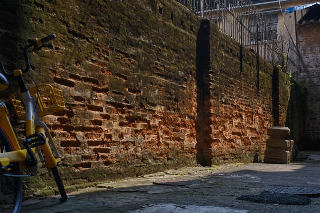 An old, moss-covered brick wall with vertical stone pillars alongside a yellow bicycle