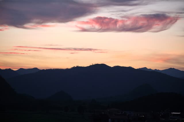 Dark mountain range silhouette against a pastel sunset sky with pink clouds