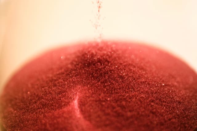 Close-up of red sand particles falling from above to form a conical mound against a blurred, light-colored background