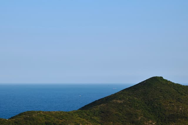 Green mountain slope, blue ocean, light blue sky
