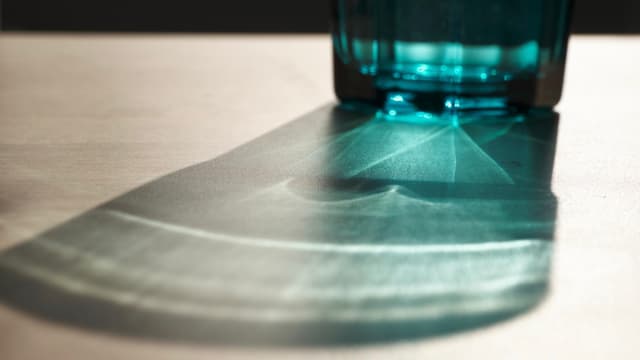 A close-up view of a blue glass object casting a translucent geometric shadow across a light-colored surface